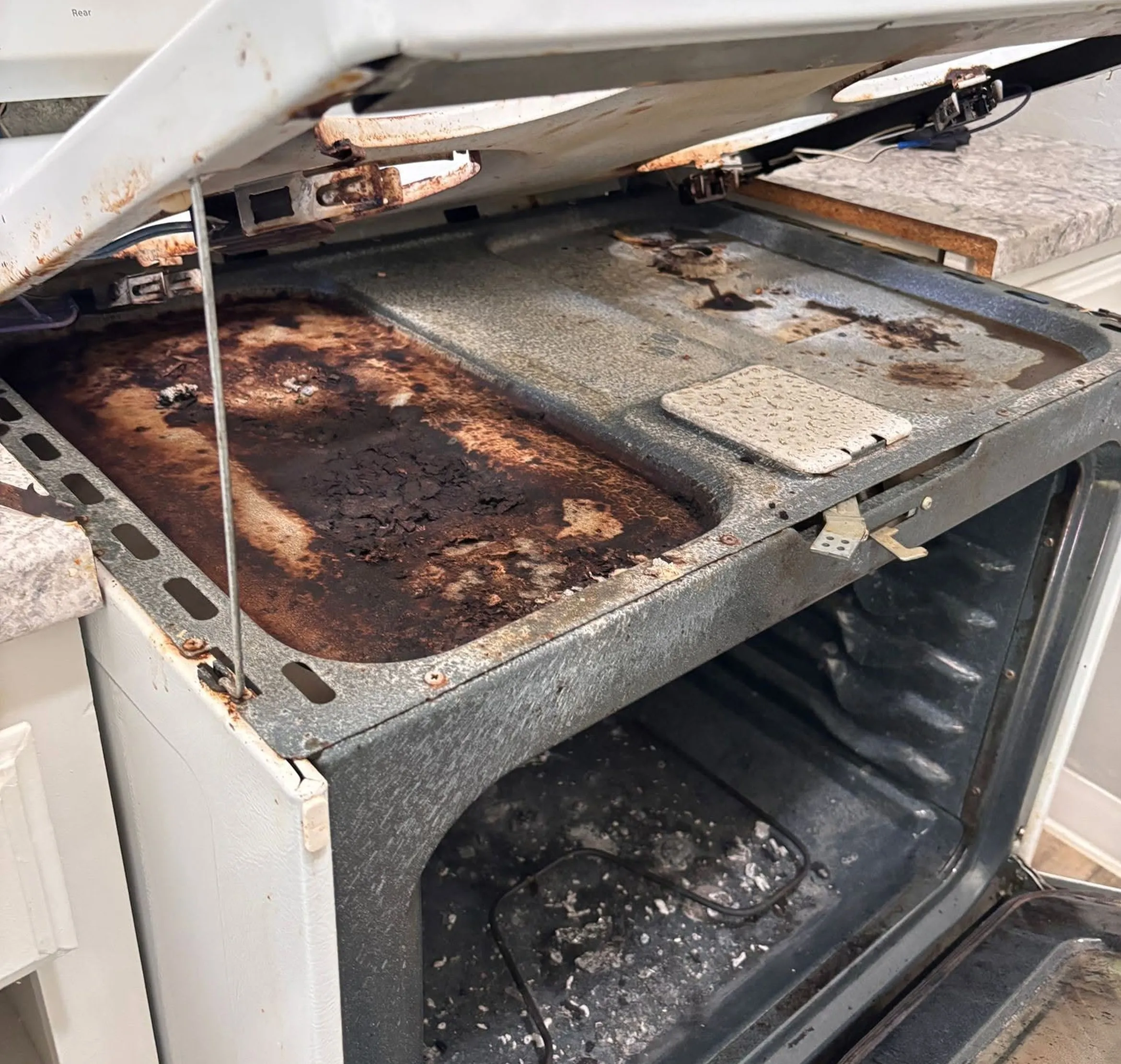 Electric range with burnt-on grease and debris under the burners and inside the oven before cleaning