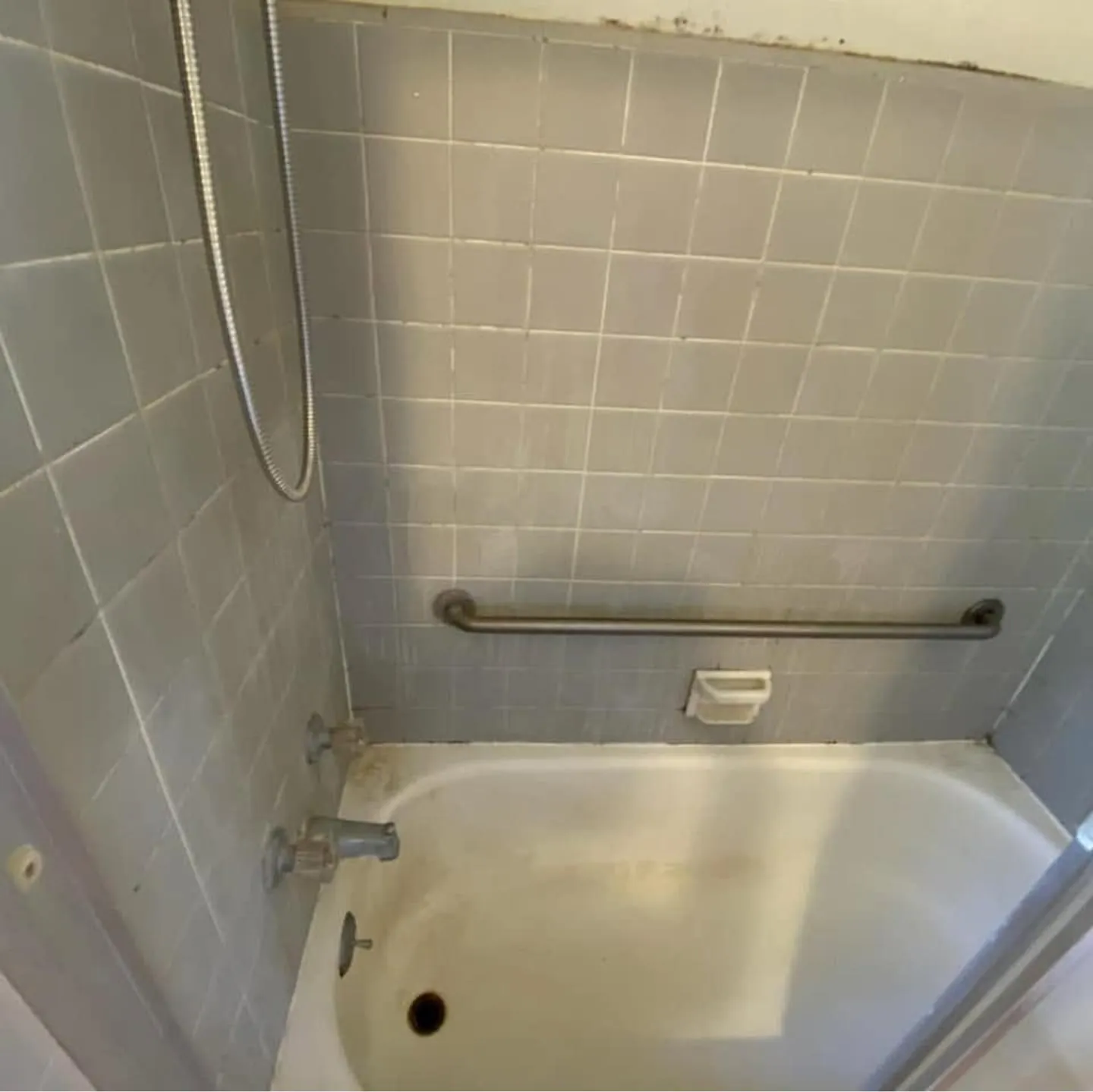 Tiled tub surround with grime on the tub and grout before cleaning