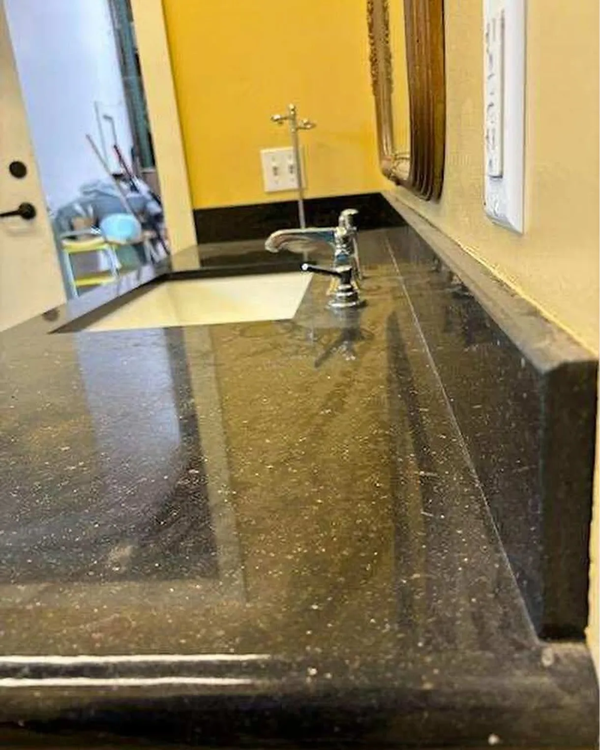 Black stone vanity counter with dust and water spots before cleaning